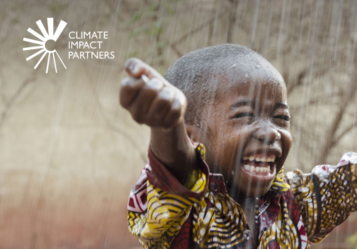 Child in colourful clothing playing under a shower | Climate Impact Partners