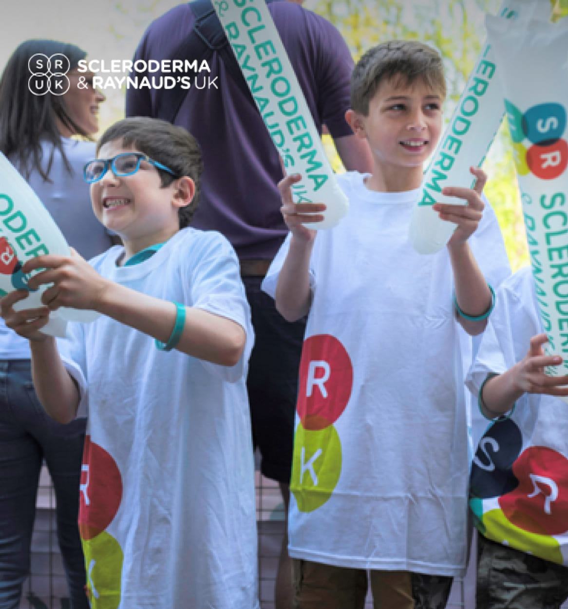Crowd of children holding Scleroderma & Raynaud's UK branding.
